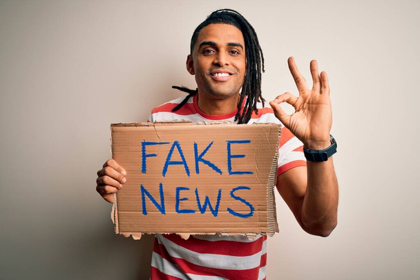 Jovem afro-americano com dreadlocks segurando banner com falso protesto mensagem de notícias fazendo sinal ok com os dedos, excelente símbolo
 - Foto, Imagem