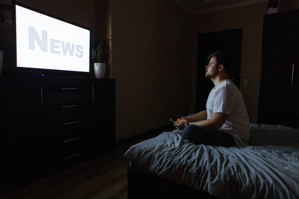 jovem adulto sentado na cama olhando TV. espaço de cópia de tela branca. tempo noturno
 - Foto, Imagem