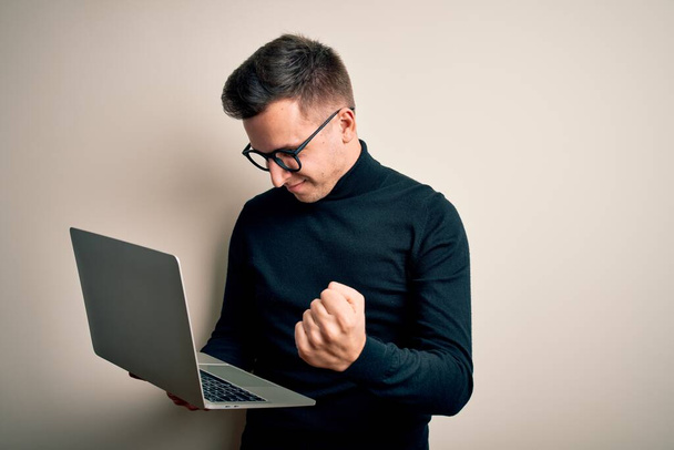 Jeune homme d'affaires caucasien beau portant des lunettes à l'aide d'un ordinateur portable ennuyé et frustré criant de colère, fou et criant avec la main levée, concept de colère
 - Photo, image