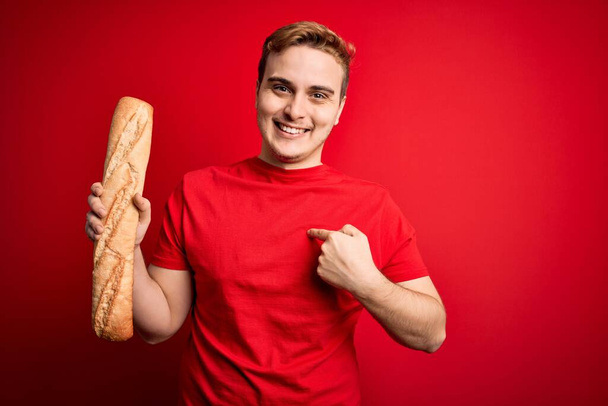 jovem bonito ruiva homem segurando fresco caseiro pão sobre isolado vermelho fundo apontando dedo para um auto sorrindo feliz e orgulhoso
 - Foto, Imagem