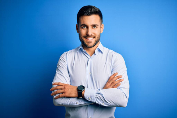 Young handsome man wearing elegant shirt standing over isolated blue background happy face smiling with crossed arms looking at the camera. Positive person. - Photo, Image
