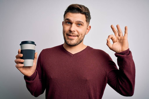 Jeune homme aux yeux bleus buvant du café à emporter bouteille en plastique sur fond isolé faisant ok signe avec les doigts, excellent symbole
 - Photo, image