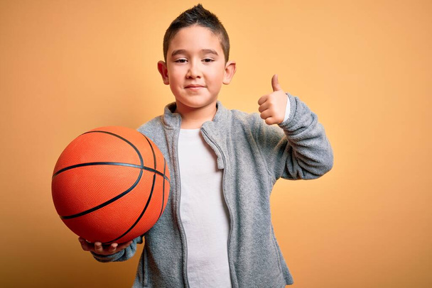 若いです男の子遊びますとともにバスケットボールゲームボール上の孤立した黄色の背景幸せなです大きな笑顔をしますokサイン,親指アップとともに指,優れたサイン - 写真・画像