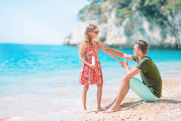 Młody tata nakłada krem na nos córki na plaży. Ochrona przeciwsłoneczna - Zdjęcie, obraz