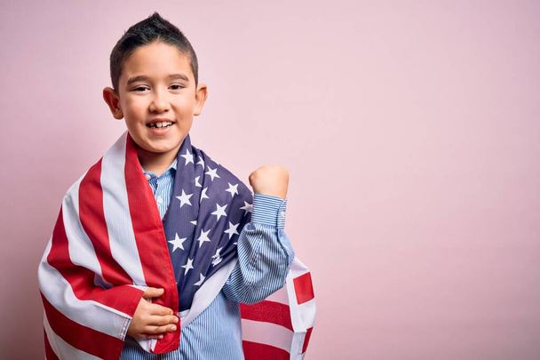 Νεαρό μικρό πατριωτικό παιδί που καλύπτεται στις Ηνωμένες Πολιτείες της Αμερικής σημαία την ημέρα της ανεξαρτησίας ουρλιάζοντας υπερήφανος και γιορτάζοντας τη νίκη και την επιτυχία πολύ ενθουσιασμένος, ζητωκραυγάζοντας συγκίνηση - Φωτογραφία, εικόνα