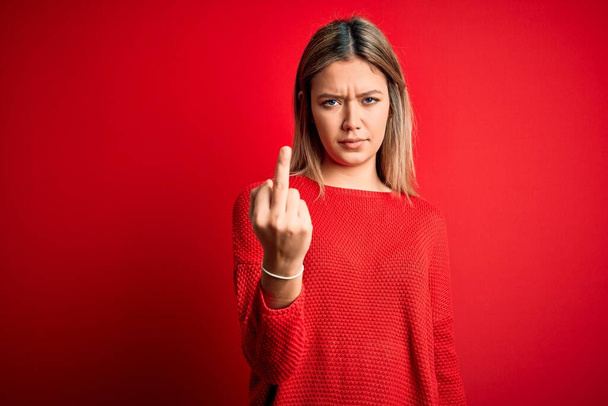 Young beautiful blonde woman wearing casual sweater over red isolated background Showing middle finger, impolite and rude fuck off expression - Φωτογραφία, εικόνα