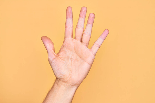 Valkoihoisen nuoren miehen käsi, jolla on sormet eristetyn keltaisen taustan päällä. Numero 5 näyttää viisi sormea. - Valokuva, kuva