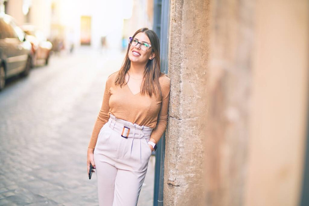 Young beautiful woman smiling happy and confident. Standing with smile on face leaning on the wall at the town street - Foto, imagen