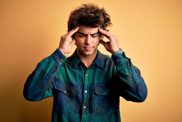 Jonge knappe man draagt casual shirt staan over geïsoleerde gele achtergrond met de hand op hoofdpijn omdat stress. Lijdende migraine. - Foto, afbeelding
