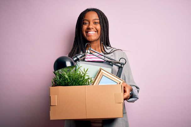 Giovane operaia afroamericana con in mano un cartone da ufficio licenziato dal lavoro d'affari con una faccia felice in piedi e sorridente con un sorriso fiducioso che mostra i denti
 - Foto, immagini