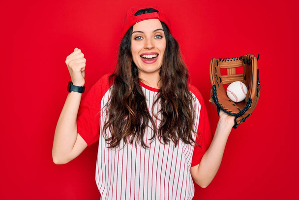 Νεαρή όμορφη αθλήτρια με μπλε μάτια που παίζει μπέιζμπολ χρησιμοποιώντας γάντι και μπάλα ουρλιάζοντας περήφανη και γιορτάζοντας τη νίκη και την επιτυχία πολύ ενθουσιασμένη, ζητωκραυγάζοντας συγκίνηση - Φωτογραφία, εικόνα
