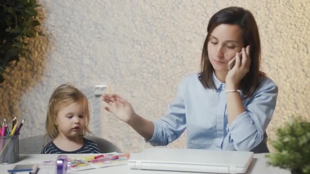 Junge Mutter streichelt Baby und telefoniert. Eine Frau im Mutterschaftsurlaub arbeitet von zu Hause aus, führt wichtige Telefonate, hält ihr Baby in der Hand und sitzt vor dem Laptop. - Filmmaterial, Video