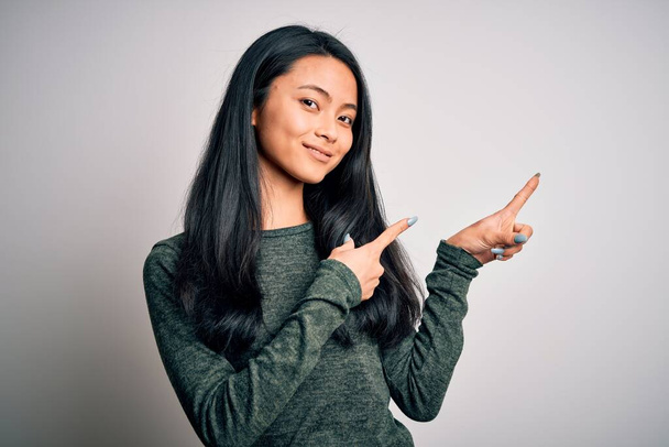 Young beautiful chinese woman wearing casual t-shirt over isolated white background smiling and looking at the camera pointing with two hands and fingers to the side. - Valokuva, kuva