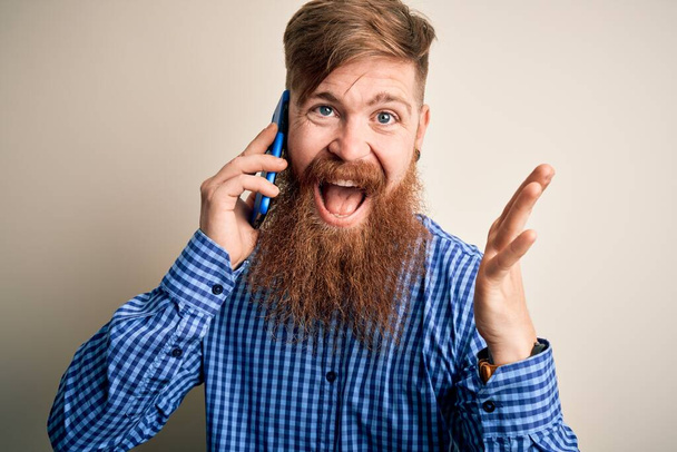 Pelirrojo irlandés con barba conversando en un teléfono inteligente sobre un fondo aislado muy feliz y emocionado, expresión ganadora celebrando la victoria gritando con una gran sonrisa y levantando las manos
 - Foto, imagen