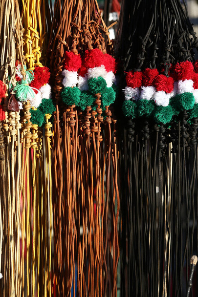 Tradycyjne skórzane bicze na sprzedaż w węgierskich kolorach narodowych. Pionowe zdjęcie. Czerwone białe i zielone kolorowe węgierskie bicze na rynku rolnym na sprzedaż - Zdjęcie, obraz