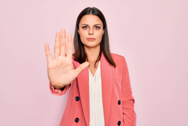 Young beautiful brunette businesswoman wearing elegant jacket over isolated pink background doing stop sing with palm of the hand. Warning expression with negative and serious gesture on the face. - Foto, afbeelding