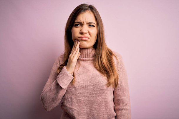 Красивая молодая женщина в свитере в водолазке на розовом изолированном фоне касается рта с болезненным выражением лица из-за зубной боли или зубной болезни на зубах. Дантист
 - Фото, изображение