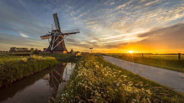 夏のフィールドで日没時にサイクリングトラックに沿ってオランダの木製風車花と美しい空 - 写真・画像