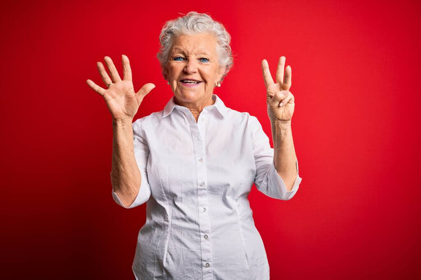 Senior beautiful woman wearing elegant shirt standing over isolated red background showing and pointing up with fingers number eight while smiling confident and happy. - Photo, Image