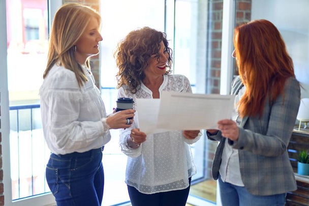 Een groep zakenvrouwen die blij zijn om samen te werken. Staande met glimlach op het gezicht lezen van documenten op kantoor - Foto, afbeelding