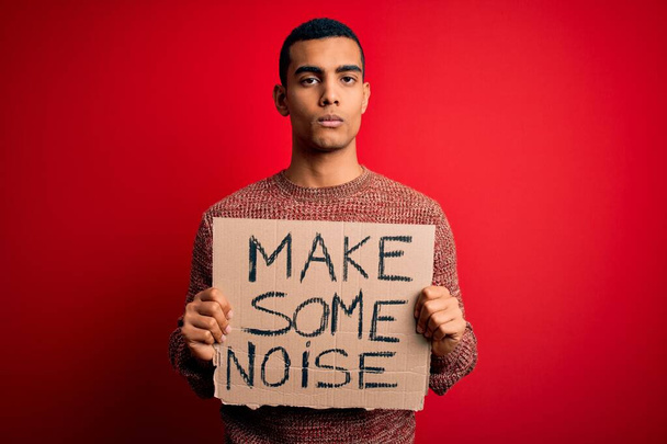 Beau militant afro-américain protestant en tenant une bannière avec faire du bruit message avec une expression confiante sur la pensée intelligente visage sérieux
 - Photo, image