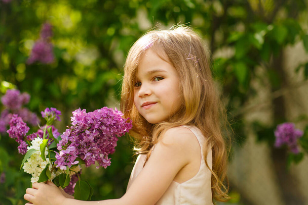 kid girl in near a lilac flowers  with bouquet - Фото, зображення