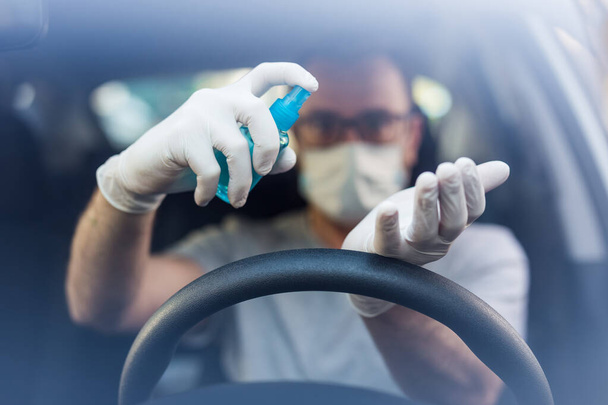 Close up of driver in protective mask with hands using alcohol hand sanitizer sprayer, covid-19 protection from bacteria and virus infection. - Photo, image