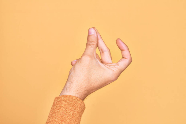 Hand of caucasian young man showing fingers over isolated yellow background snapping fingers for success, easy and click symbol gesture with hand - Фото, изображение