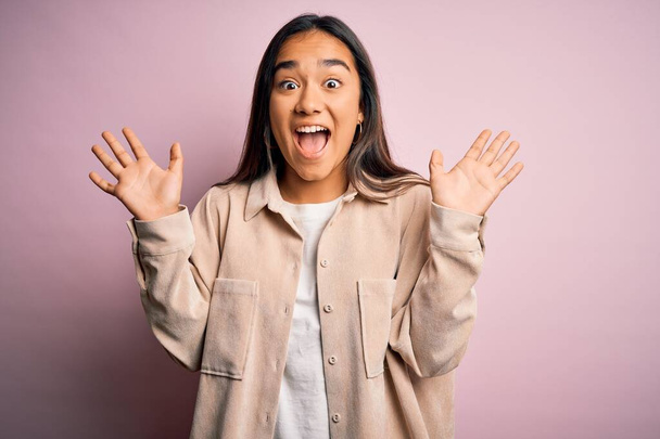 Young beautiful asian woman wearing casual shirt standing over pink background celebrating crazy and amazed for success with arms raised and open eyes screaming excited. Winner concept - Foto, imagen