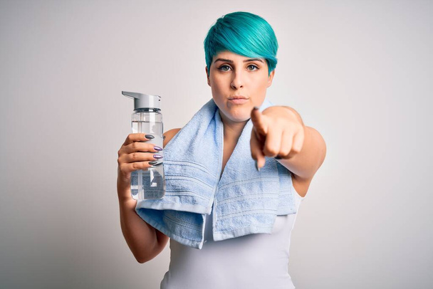 Jonge sportieve vrouw met blauw haar in de mode fles water dragen handdoek na sport wijzen met de vinger naar de camera en naar u, handteken, positieve en zelfverzekerde gebaar van de voorkant - Foto, afbeelding