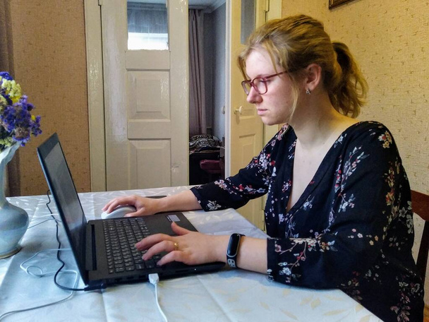 Серйозна молода жінка з Єврозони сидить за столом і працює вдома на ноутбуку. - Фото, зображення