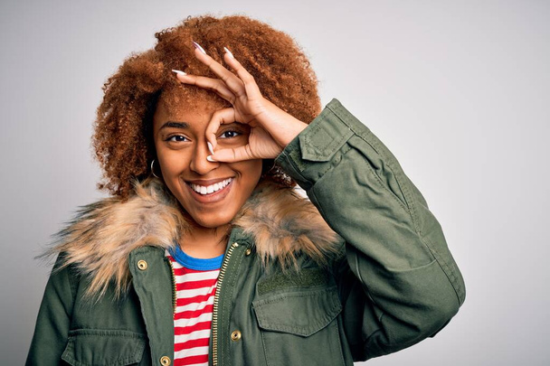 Nuori kaunis Afrikkalainen Amerikan afro nainen kihara tukka yllään rento talvi takki onnellinen kasvot hymyillen tekee ok merkki käsin katsellen sormien läpi
 - Valokuva, kuva