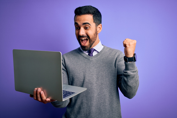 Nuori komea liikemies parta työskentelee kannettavan tietokoneen yli violetti tausta huutaa ylpeä ja juhlii voittoa ja menestystä erittäin innoissaan, hurraavat tunteet
 - Valokuva, kuva