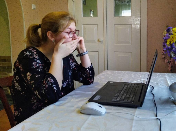 Mujer joven europea asustada sentarse en la mesa, hablar en el teléfono inteligente y trabajar en el ordenador portátil en casa
 - Foto, imagen