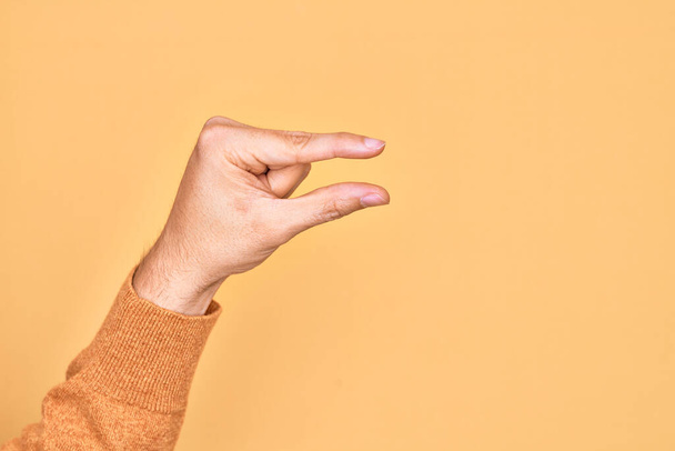 Mano de joven caucásico mostrando los dedos sobre el fondo amarillo aislado recogiendo y tomando cosa invisible, sosteniendo el objeto con los dedos mostrando el espacio - Foto, imagen