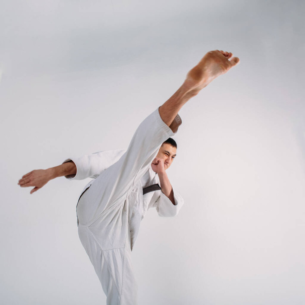 Молодой сильный парень, карате в белом кимоно в студии на белом фоне выполняет удар
 - Фото, изображение