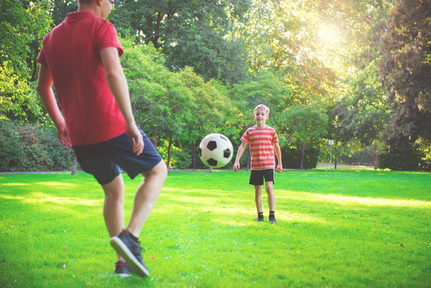 Happy young father play with his little son football in green sunny park - 写真・画像