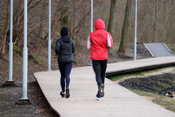 Couple running in a spring park during quarantine, rear view. Concept of workout, people runners, slimming in cold season - Foto, afbeelding
