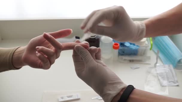 Egy orvos kesztyűs kézzel vesz vért az ujjáról, hogy elemezze egy lány betegét. Közelkép. - Felvétel, videó