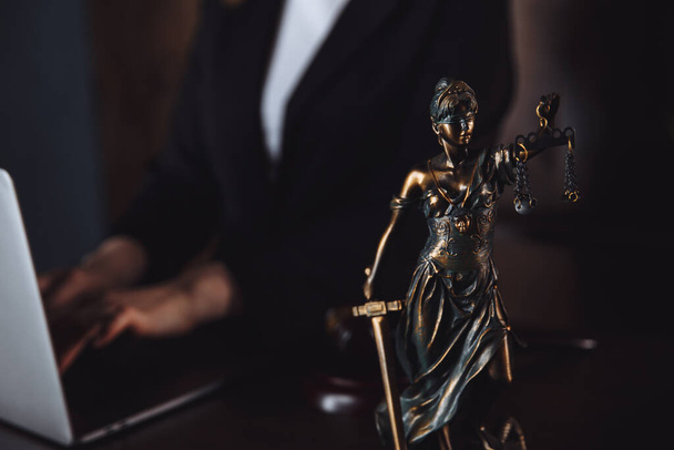 Юридический офис. Статуя правосудия с весами и адвокатом, работающим над ноутбуком. Юридическое право, консультации и правосудие
. - Фото, изображение