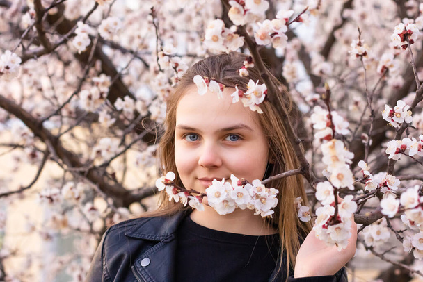 Portrait of hipster girl standing in spring blossom flowers garden and look at camera. Beautiful happy young woman enjoying smell in a flowering springtime vocation. - Foto, imagen