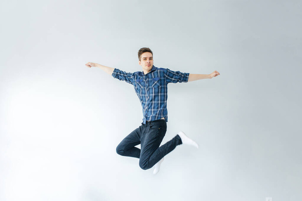 Νεαρός με μπλε πουκάμισο και μαύρο παντελόνι πηδάει σε ανοιχτό γκρι φόντο - Φωτογραφία, εικόνα
