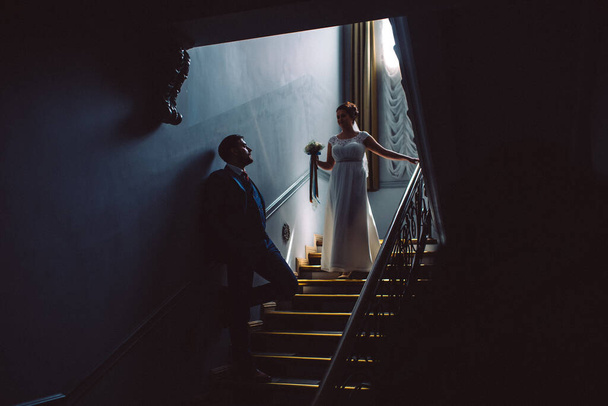 A wedding couple, they are standing on the steps, a man is standing against the wall and the girl is going down the steps - Φωτογραφία, εικόνα