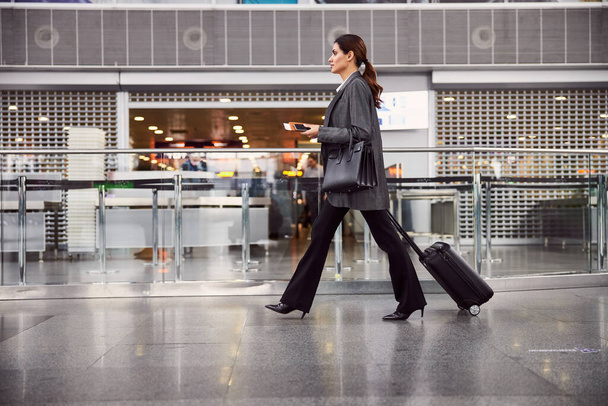 Beautiful young woman with luggage walking in airport - 写真・画像