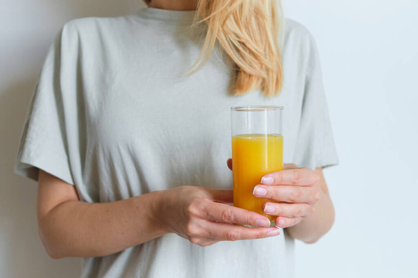 Girl holds a glass of orange juice in her hands. Fresh natural orange juice. Vitamin drink for breakfast. Healthy lifestyle, organic diet. Refreshment after morning fitness. Enjoy delicious beverage - 写真・画像