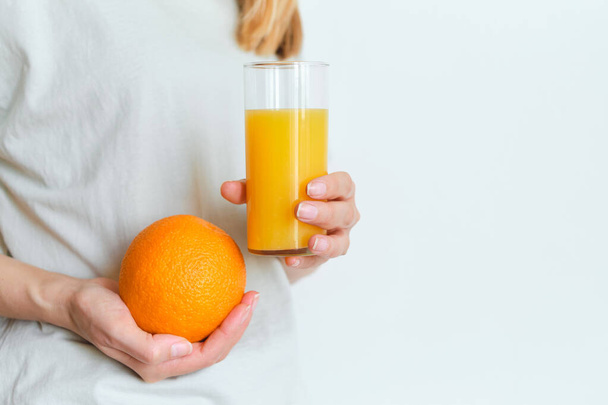 Girl holds a glass of orange juice in her hands. Fresh natural orange juice. Vitamin drink for breakfast. Healthy lifestyle, organic diet. Refreshment after morning fitness. Enjoy delicious beverage - Fotó, kép