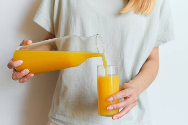 Girl holds a glass of orange juice in her hands. Fresh natural orange juice. Vitamin drink for breakfast. Healthy lifestyle, organic diet. Refreshment after morning fitness. Enjoy delicious beverage - Фото, изображение