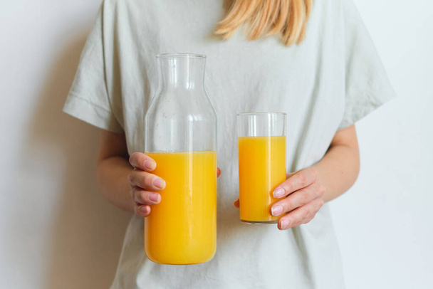 Girl holds a glass of orange juice in her hands. Fresh natural orange juice. Vitamin drink for breakfast. Healthy lifestyle, organic diet. Refreshment after morning fitness. Enjoy delicious beverage - Foto, Imagen