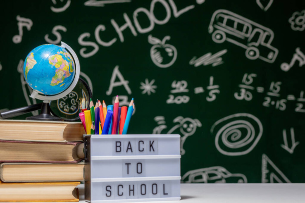 Back to school background with books, pencils and globe on white table on a green blackboard background - Photo, image