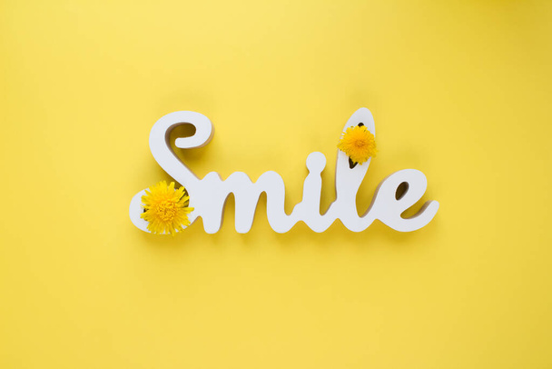 Het woord SMILE versierd met gele paardebloemen op felgele achtergrond met copyspace - Foto, afbeelding